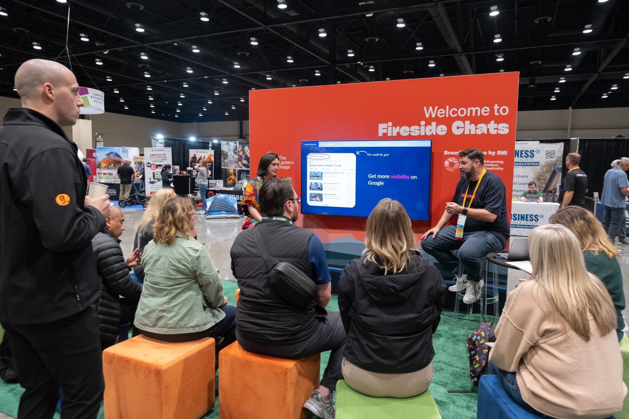 Attendees sitting on ottomans, focused on a Fireside chat on the expo floor